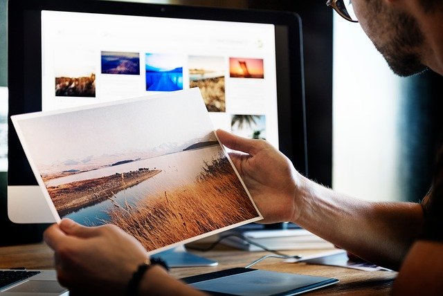 Person at a computer looking at images and holding a photograph.